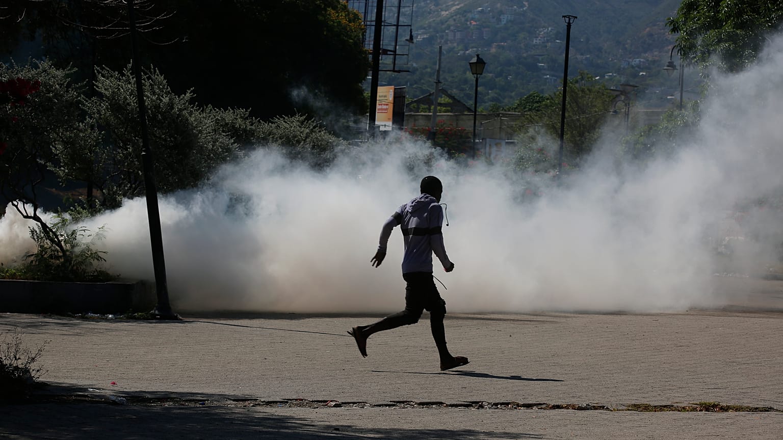 A man runs for cover as riot police launch tear gas in an effort to remove street vendors in Port-au-Prince, Haiti, Tuesday, April 2, 2024.