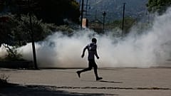 A man runs for cover as riot police launch tear gas in an effort to remove street vendors in Port-au-Prince, Haiti, Tuesday, April 2, 2024.