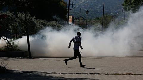 A man runs for cover as riot police launch tear gas in an effort to remove street vendors in Port-au-Prince, Haiti, Tuesday, April 2, 2024.