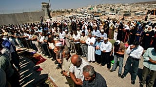 مصلون فلسطينيون يصلون خلف المتاريس عند حاجز قلنديا بين مدينة رام الله بالضفة الغربية والقدس