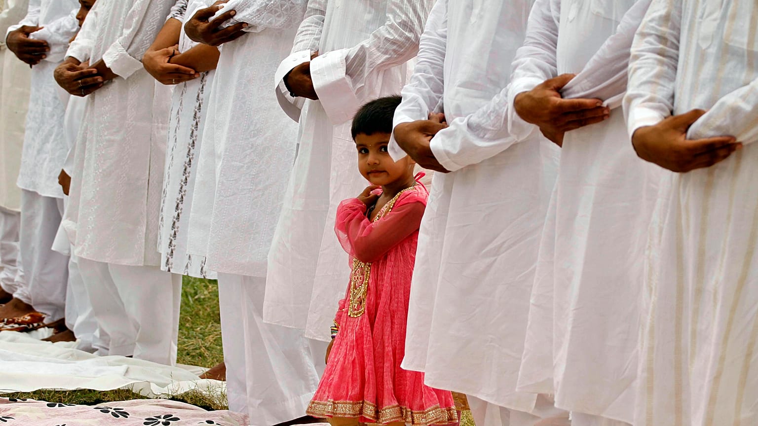 A Muslim girl looks on as elders offer prayers during Eid al-Fitr in Allahabad, India