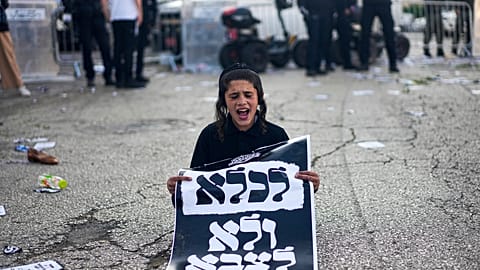 An ultra-Orthodox Jewish boy holds a sign reading in Hebrew, "To jail and not to army," during a protest on Thursday, April 11, 2024.