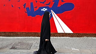 Uma mulher passa por um novo mural anti-EUA na parede da antiga embaixada dos EUA em Teerão, 2019. 