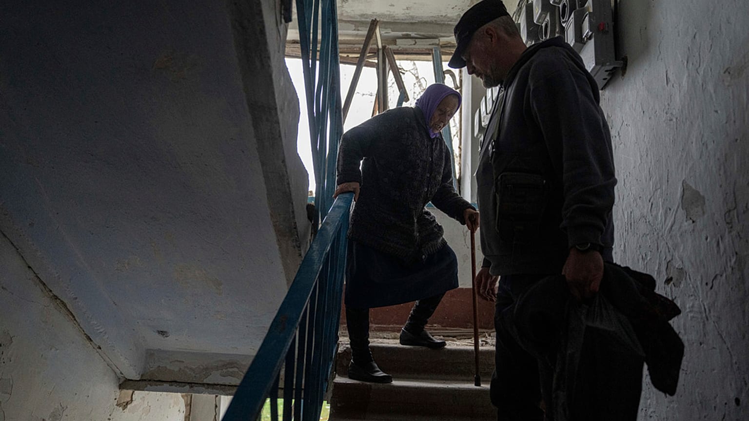Um voluntário ajuda Olga, 79 anos, a descer as escadas do seu apartamento, que foi fortemente danificado por um ataque aéreo russo