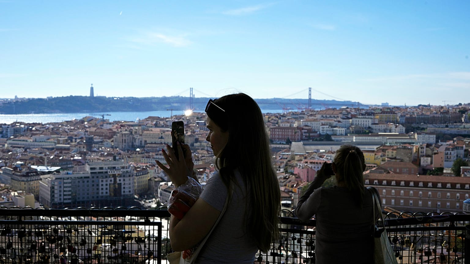Turistas tiram fotografias do miradouro de Nossa Senhora do Monte, com vista para o rio Tejo e para a baixa de Lisboa, num dia de sol quente.