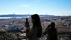 Turistas tiram fotografias do miradouro de Nossa Senhora do Monte, com vista para o rio Tejo e para a baixa de Lisboa, num dia de sol quente.