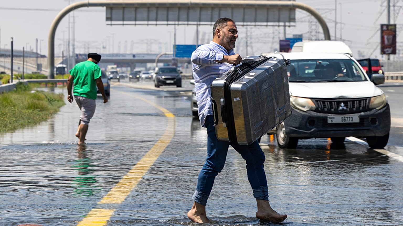 A man carries luggage through floodwater caused by heavy rain while waiting for transportation in Dubai, United Arab Emirates on Thursday
