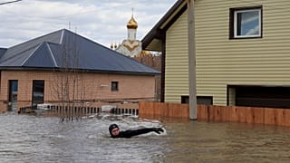 A local resident swims in the flooded street between houses in Orenburg, Russia