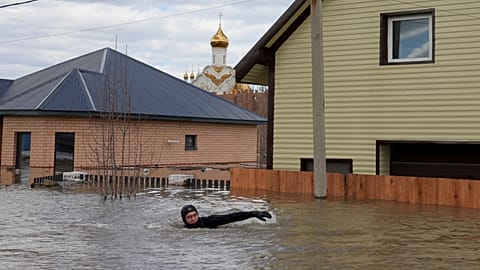 A local resident swims in the flooded street between houses in Orenburg, Russia