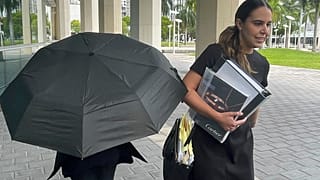 La famosa diseñadora de bolsos Nancy González se esconde bajo un paraguas mientras camina con su abogada Andrea López fuera de la corte federal el lunes 22 de abril de 2024, en Miami.