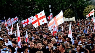 Kormánypárti tüntetők grúz nemzeti zászlóval az „ügynöktörvényt" támogató gyűlésen Tbilisziben, 2024. április 29-én.