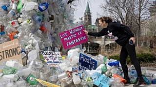 Activist Dianne Peterson places a sign on an art installation outside a United Nations conference on plastics.