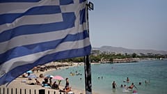 People enjoy the sea as a Greek flag waves at Alimos beach,