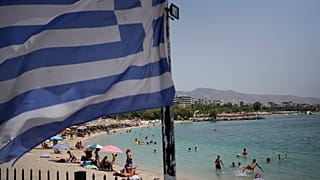 People enjoy the sea as a Greek flag waves at Alimos beach,