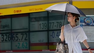 A woman walks across an intersection near monitors showing Japan's Nikkei 225 index and a foreign exchange rate of the Japanese yen against the U.S. dollar in Tokyo