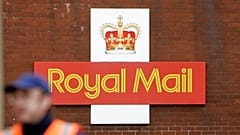 A British Royal Mail logo is seen behind a postal worker walking at a delivery office in London, Monday, Oct. 19, 2009. 