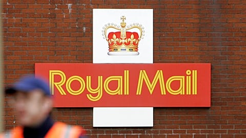 A British Royal Mail logo is seen behind a postal worker walking at a delivery office in London, Monday, Oct. 19, 2009. 