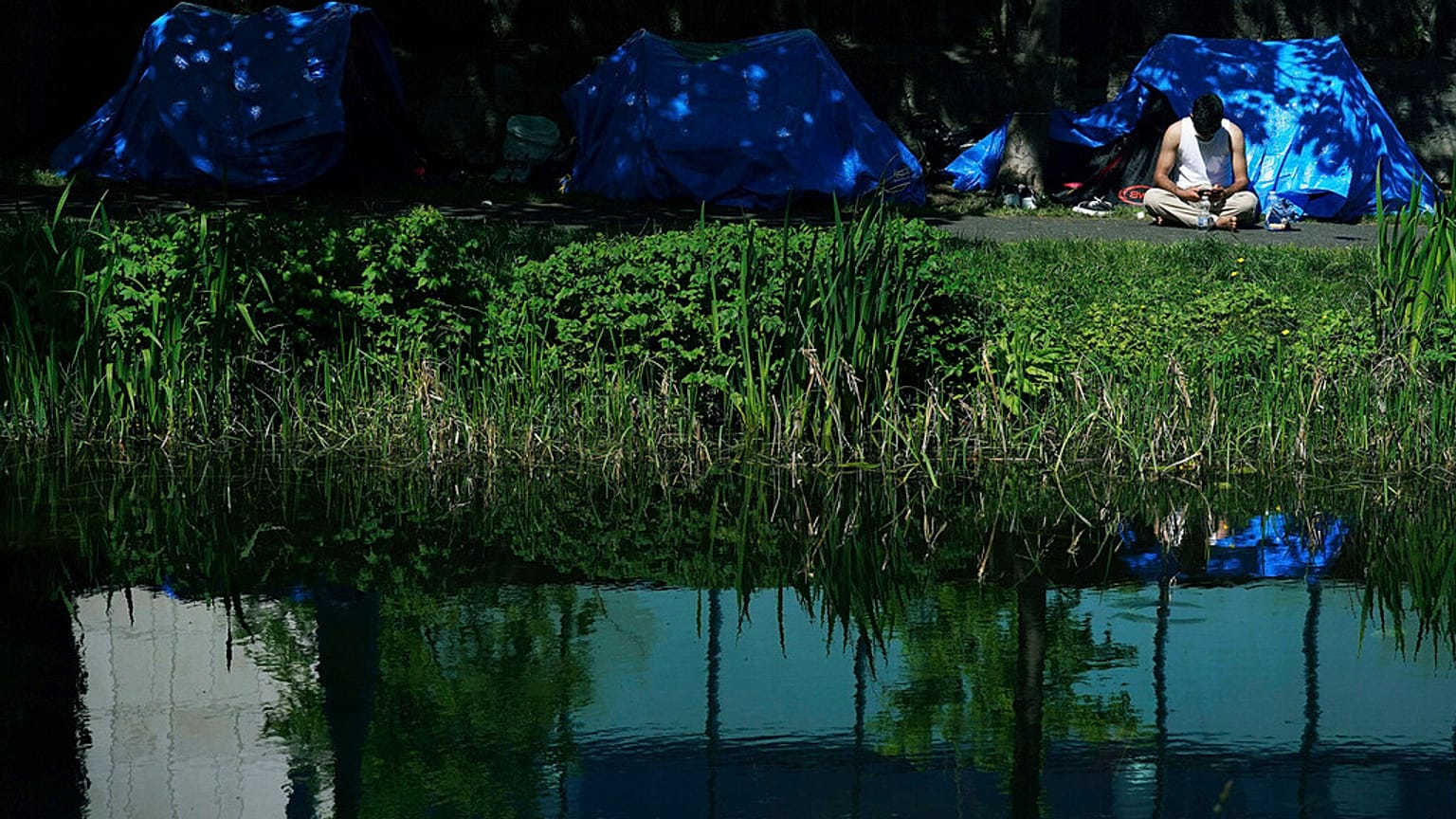 A man sits outside one of the dozens of tents which have been pitched by migrants along a stretch of the Grand Canal, in Dublin, Sunday May 5, 2024.