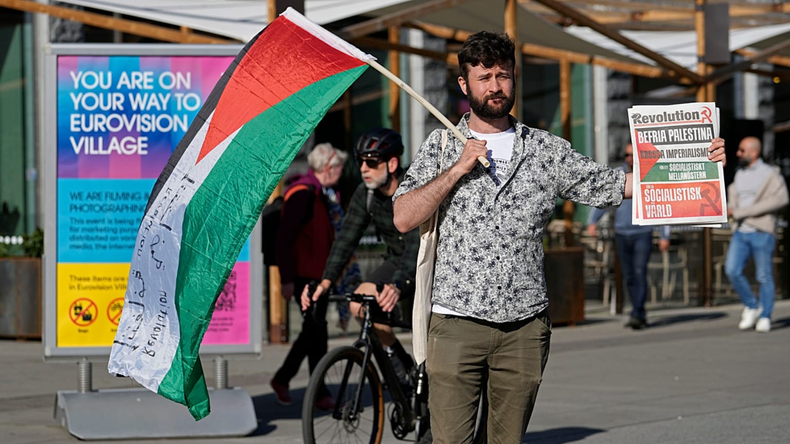 Un ciudadano lleva una bandera palestina y un cartel de protesta.