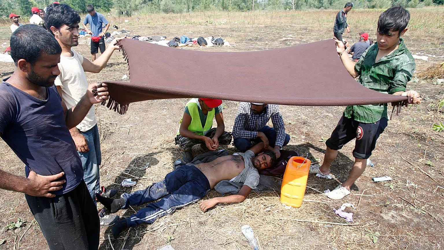 A migrant is helped after he fainted from exhaustion at a makeshift camp for migrants in Horgos, Serbia, July 27, 2016.