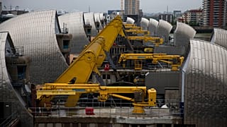 Yellow rocking beams stand raised as the rising sector gates of the Thames Barrier.