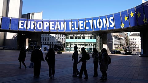 A group stands under an election banner outside the European Parliament in Brussels on April 29, 2024. 