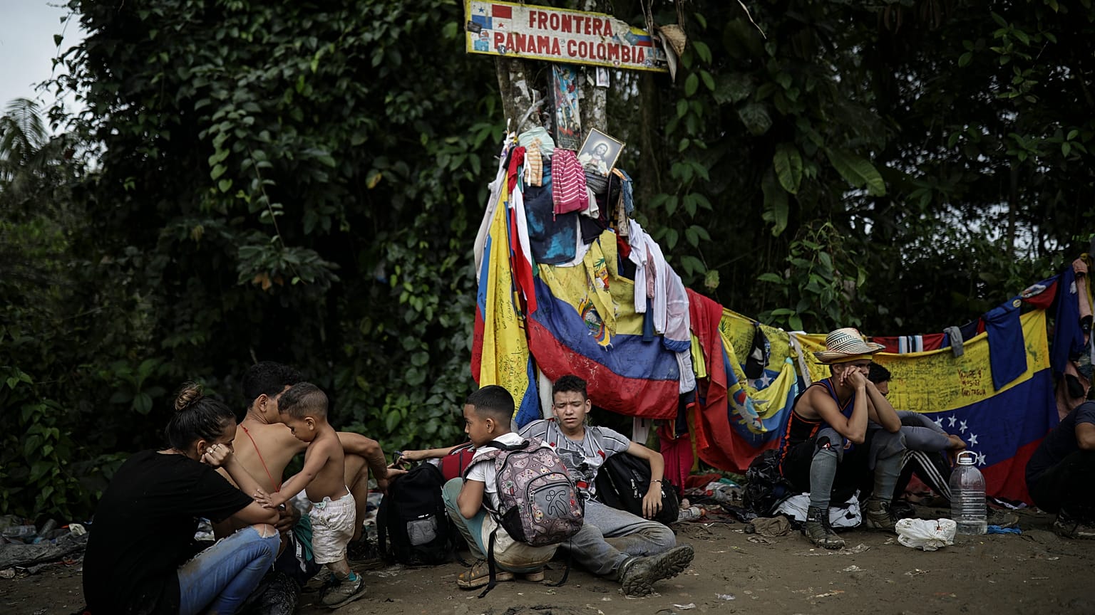 Migrantes sentados bajo una señal que marca la frontera entre Panamá y Colombia durante su travesía por el Tapón del Darién.