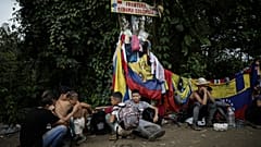 Migrantes sentados bajo una señal que marca la frontera entre Panamá y Colombia durante su travesía por el Tapón del Darién.