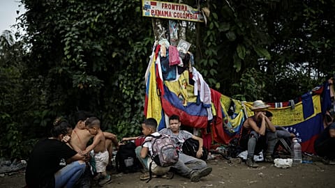 Migrants sit under a sign marking the Panama-Colombia border during their trek across the Darien Gap
