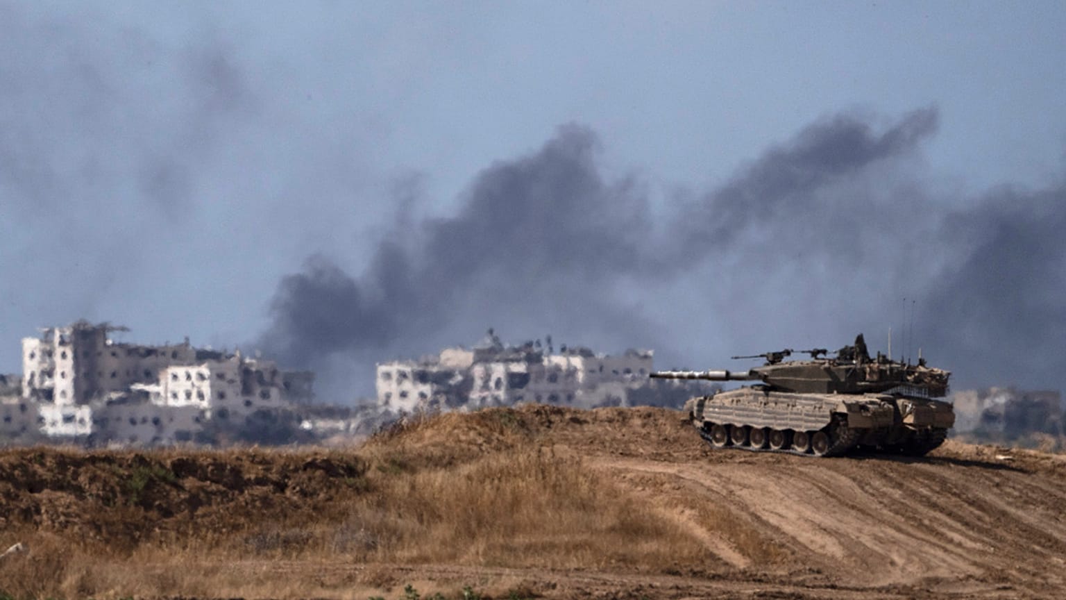 Gazze sınırında bulunan bir İsrail tankı ve kentin içinde bombardıman sonrası yükselen siyah dumanlar