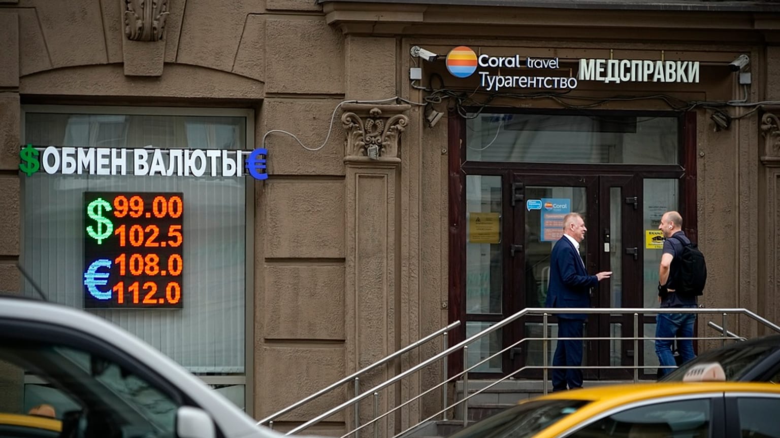 Two men talk to each other at the entrance of a currency exchange office in Moscow, Russia