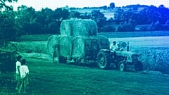 Two young children watch a local farmer transport bales of hay to his barn, August 2001