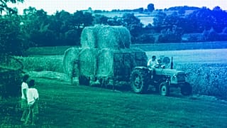 Two young children watch a local farmer transport bales of hay to his barn, August 2001