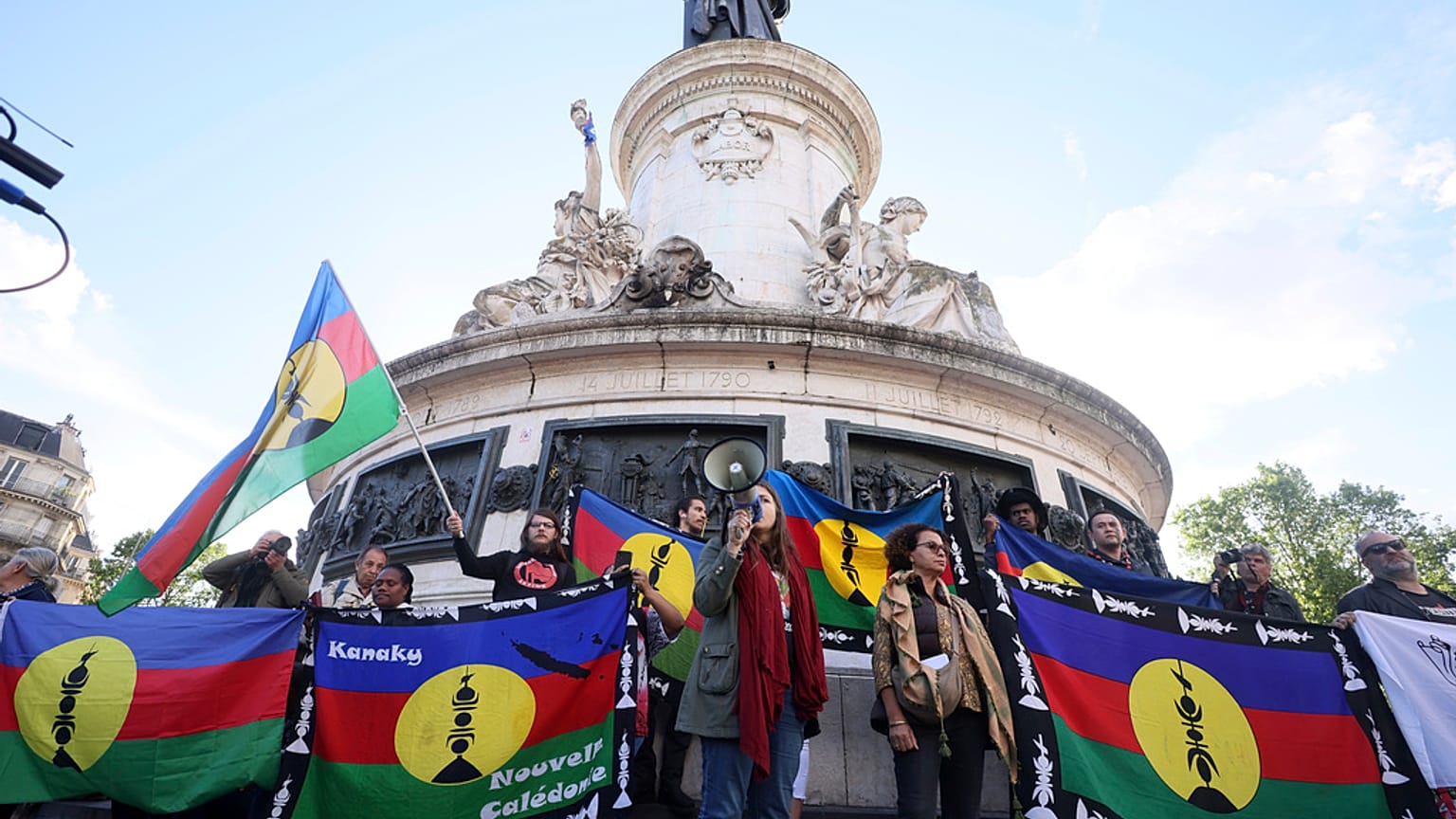 Manifestantes seguram bandeiras do Kanak e da Frente Socialista de Libertação Nacional (FLNKS) durante uma concentração em Paris