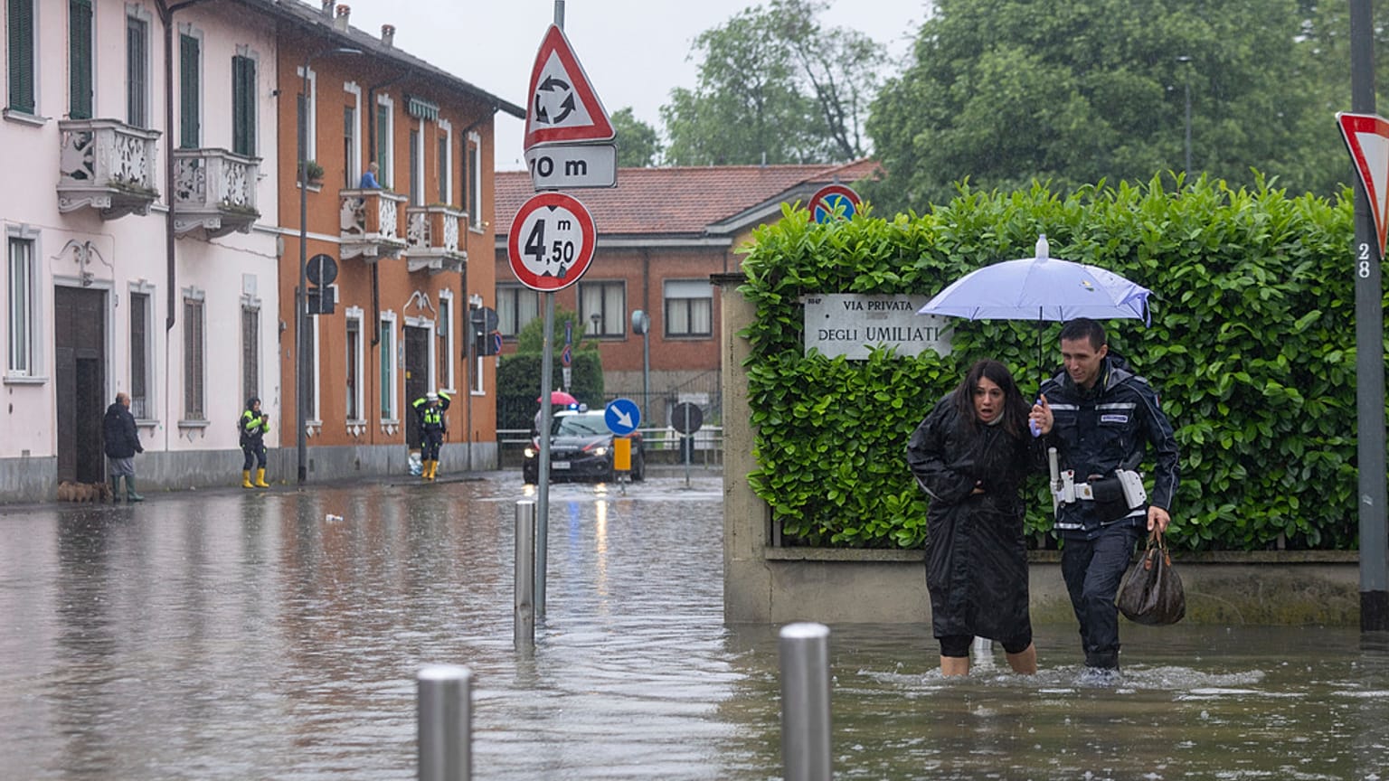 A city police officer, right, helps a woman cross a road after part of the city was flooded following persistent rains, in Milan, Italy, Wednesday, May 15, 2024 