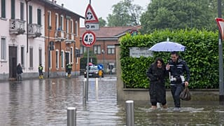 A city police officer, right, helps a woman cross a road after part of the city was flooded following persistent rains, in Milan, Italy, Wednesday, May 15, 2024 