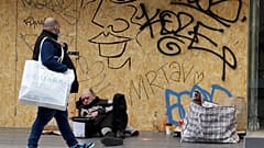 Un hombre que lleva una bolsa de compras pasa junto a un hombre sin hogar en el suelo junto a una tienda cerrada en Oxford Street en Londres, el lunes 12 de abril de 2021.
