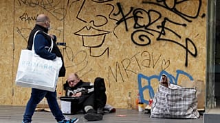 Un hombre que lleva una bolsa de compras pasa junto a un hombre sin hogar en el suelo junto a una tienda cerrada en Oxford Street en Londres, el lunes 12 de abril de 2021.