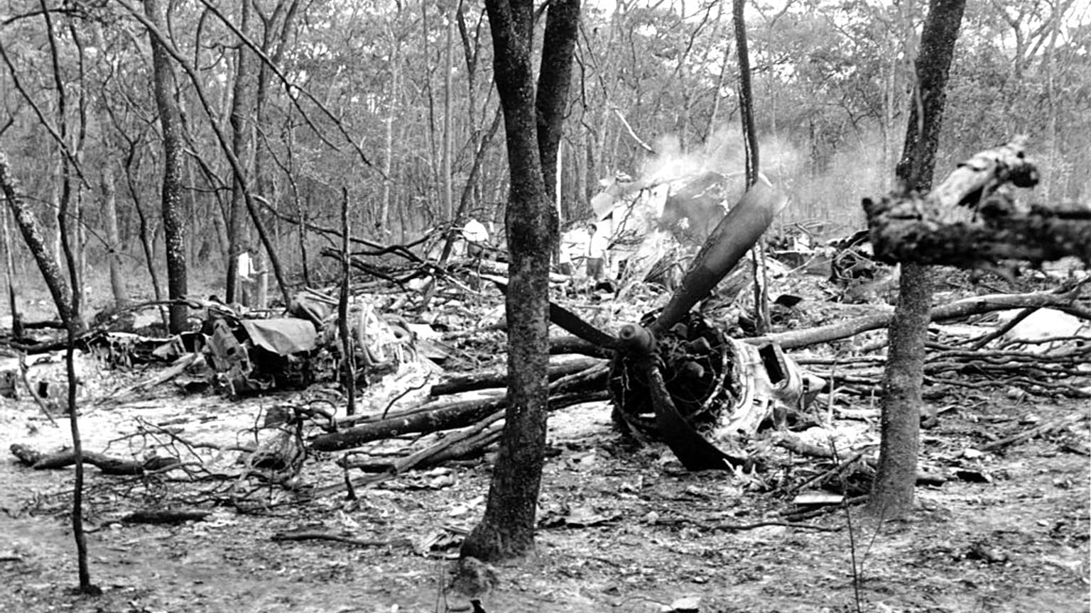 ARCHIVO - En esta foto de archivo del 19 de septiembre de 1961, buscadores caminan entre los restos dispersos de un avión DC6B en un bosque cerca de Ndola, Zambia.