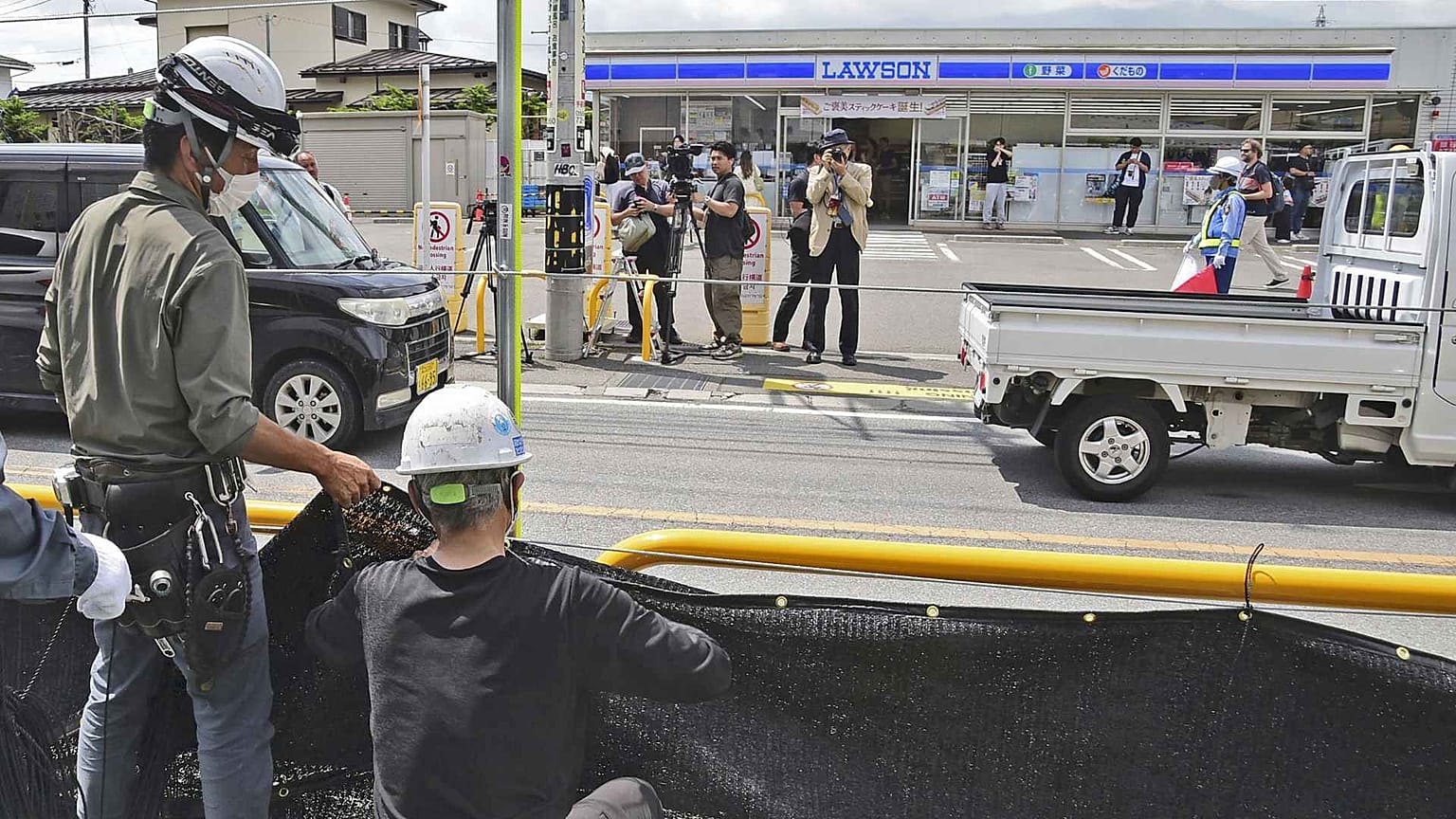 Des ouvriers installent un immense écran noir sur un trottoir de la ville de Fujikawaguchiko, dans la préfecture de Yamanashi, au centre du Japon, le mardi 21 mai 2024. 