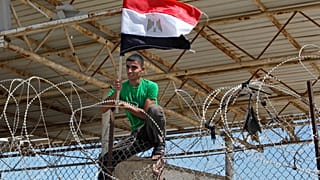  فلسطيني يتسلق سياجًا رفع عليه العلم المصري خلال مظاهرة تطالب مصر بإعادة فتح معبر رفح الحدودي في رفح، جنوب قطاع غزة، الاثنين، 16 سبتمبر، 2013.