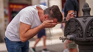 Um homem refresca-se numa fonte durante um dia quente e solarengo de verão em Madrid, Espanha.