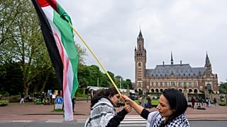 Két tüntető lengeti a palesztin zászlót a Nemzetközi Bíróságnak (Világbíróság) otthont adó Békepalota előtt Hágában, 2024 májusában.