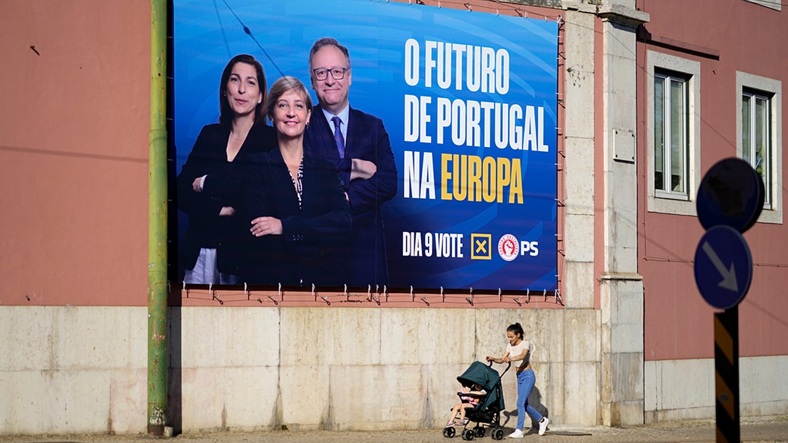 Una mujer empuja y su bebé pasan junto a una valla publicitaria del Partido Socialista para las elecciones europeas, en Lisboa, el viernes 31 de mayo de 2024.
