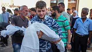 أب يحمل جثمان طفله بعد قصف إسرائيلي في دير البلح.