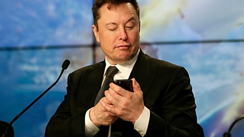Elon Musk pretends to search for an answer to a question on a cell phone during a news conference, January 2020.