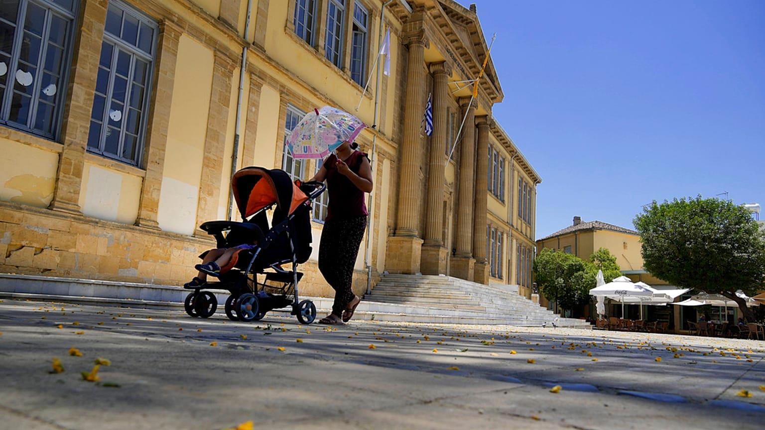 Una donna si protegge dal sole con un ombrello mentre spinge un bambino in un passeggino durante una giornata calda a Nicosia, Cipro, 4 giugno 2024