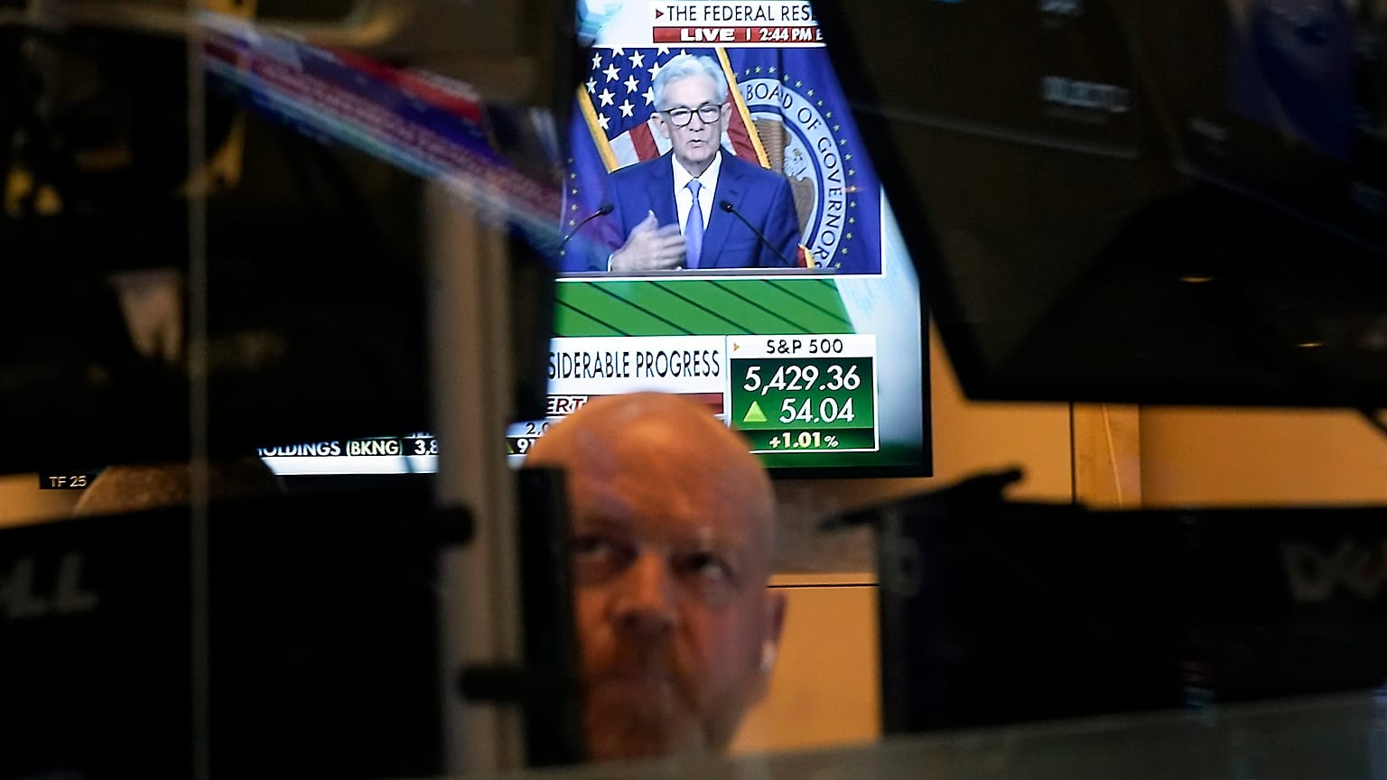 Federal Reserve Chairman Jerome Powell is framed by a trader's screens on the floor of the New York Stock Exchange 
