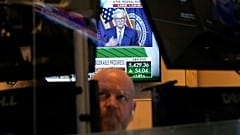 Federal Reserve Chairman Jerome Powell is framed by a trader's screens on the floor of the New York Stock Exchange 