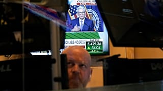 Federal Reserve Chairman Jerome Powell is framed by a trader's screens on the floor of the New York Stock Exchange